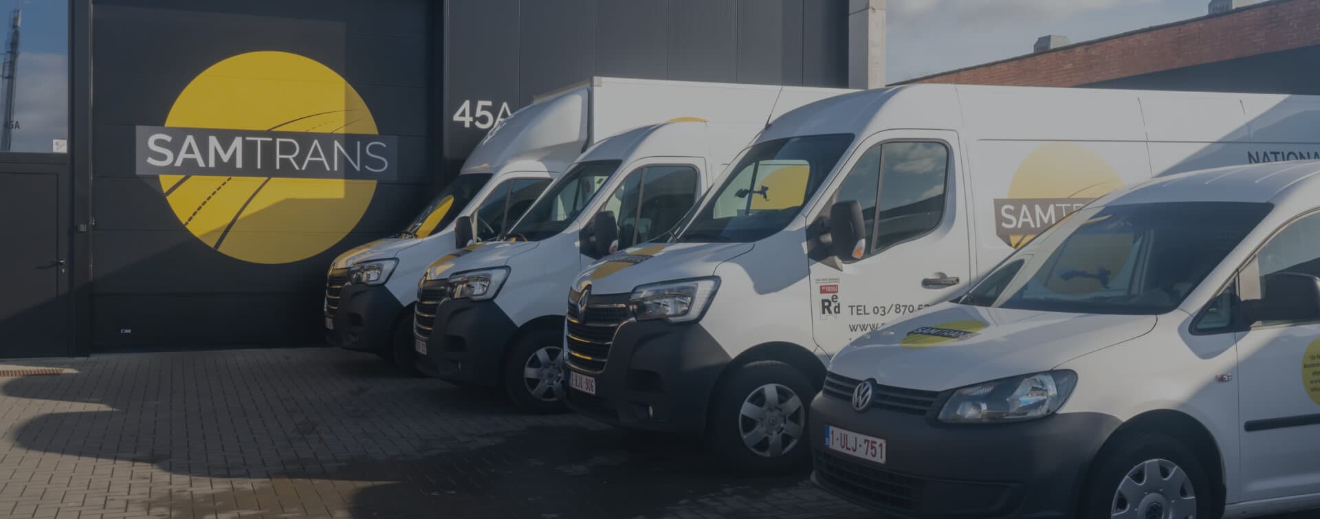 Overzicht van alle wagentypes van SamTrans Sneltransporten geparkeerd voor de poort van het bedrijf met groot logo zichtbaar.