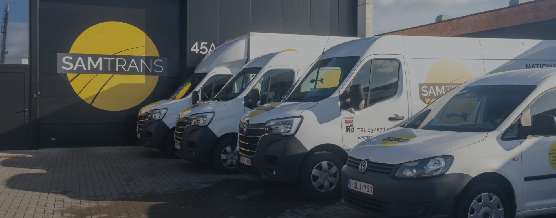 Overzicht van alle wagentypes van SamTrans Sneltransporten geparkeerd voor de poort van het bedrijf met groot logo zichtbaar.